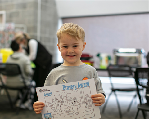 young boy holding bravery award after immunisations