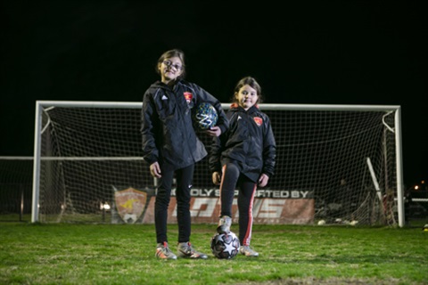 Two young soccer players stand on a field smiling at the camera
