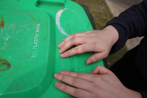 Hands touching and reading a braille sticker on the top of their bin