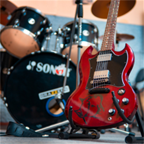 A close up image of a red electric guitar with a drum kit in the background