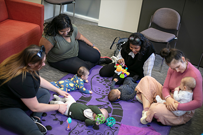 A group of parents and carers sit on a mat playing with their babies.