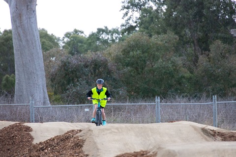 A boy confidently riding a bike along a dirt track.