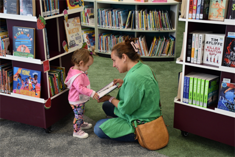 Mother and child reading a book surrounded by bookshelves at Mernda Library